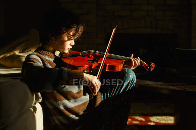 Un hermoso niño se sienta en un parche de luz solar tocando un violín rojo - foto de stock