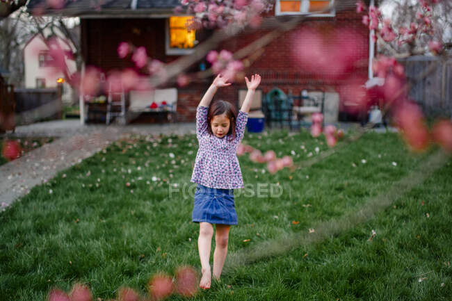 Una niña se prepara para hacer el pie de manos bajo un árbol floreciente al atardecer - foto de stock