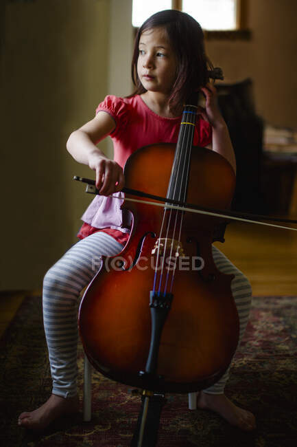 Una niña con una celda descalza en su sala de estar - foto de stock