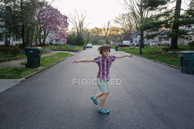 Un niño feliz gira con los brazos en una calle al atardecer en primavera - foto de stock