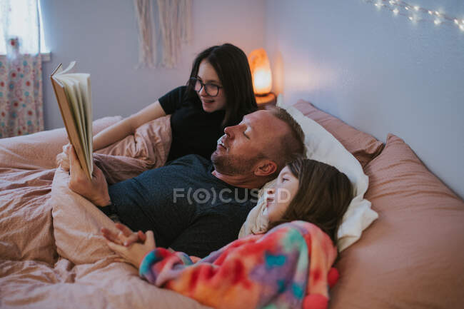 Horizontal image of family reading a book in bed — Stock Photo