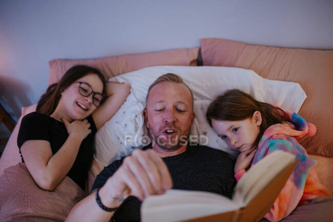 Overhead of father in bed reading with daughters — Stock Photo
