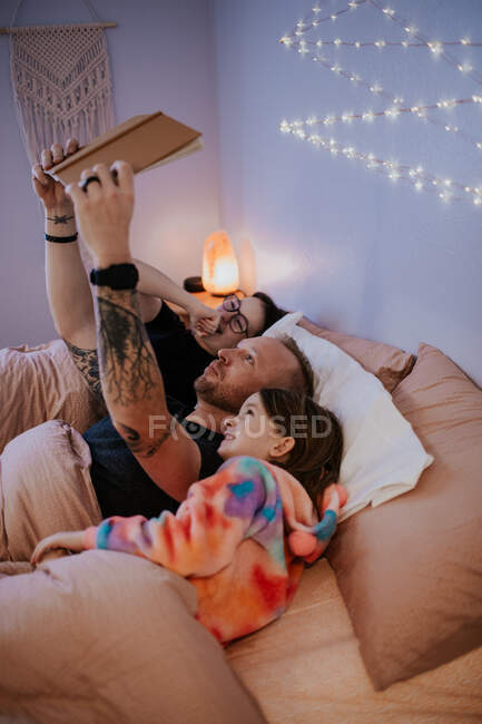 Vertical image of father laying in bed reading to kids — Stock Photo