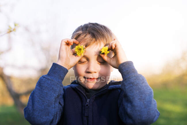 Un petit garçon jouant avec des fleurs de pissenlit au coucher du soleil. — Photo de stock