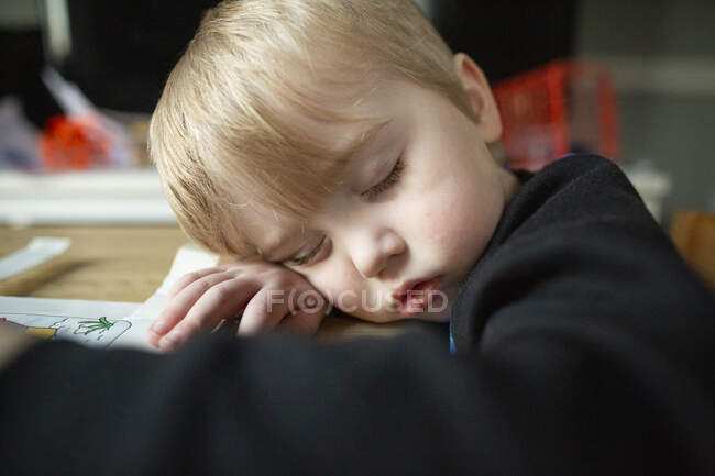 Крупним планом милий хлопчик-малюк спить з головою, спить на руку за столом — стокове фото
