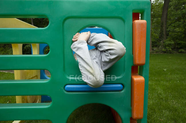 Las rodillas manchadas de hierba del niño mientras trepan a través de un juguete plástico al aire libre - foto de stock