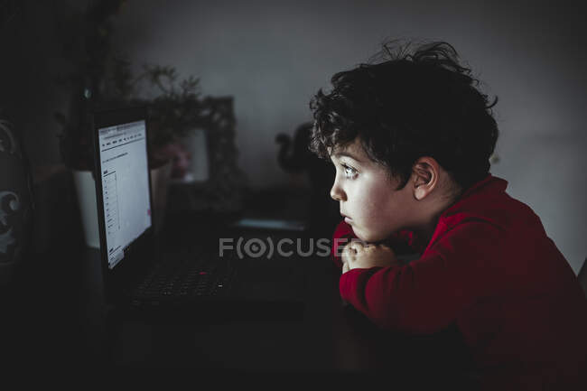 Garçon regardant ordinateur portable dans la chambre noire — Photo de stock