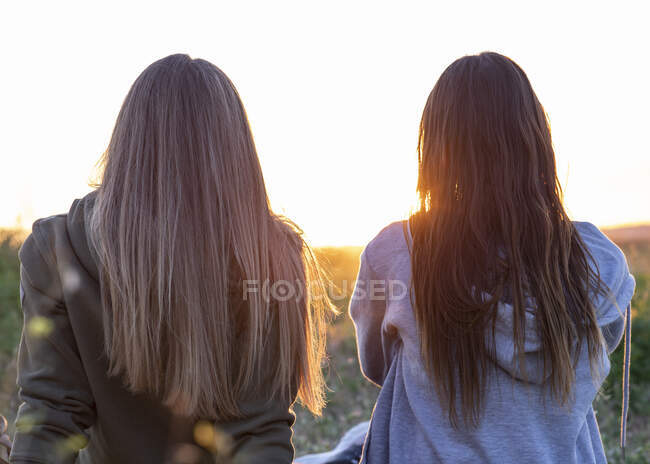 Dos chicas espalda con espalda viendo el atardecer - foto de stock