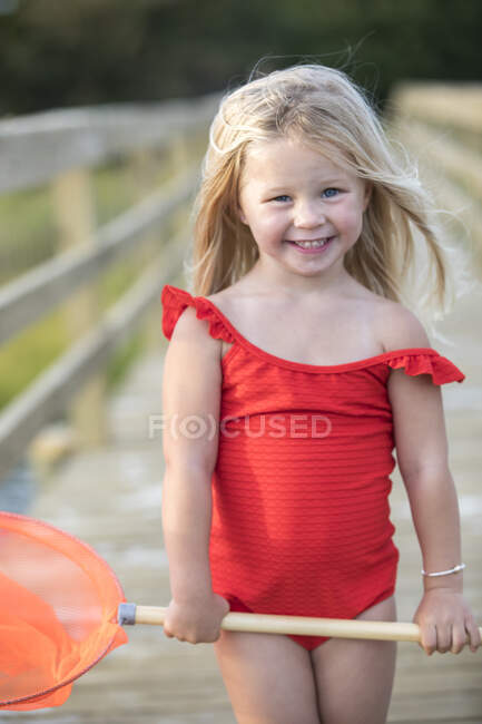 Menina em terno de banho vermelho na ponte segurando rede de pesca vermelha — Fotografia de Stock