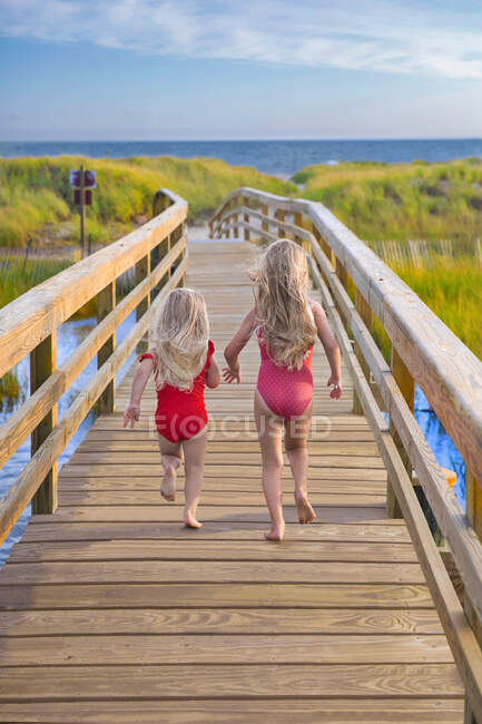 Kleine Mädchen rennen von hinten auf Brücke zum Strand — Stockfoto