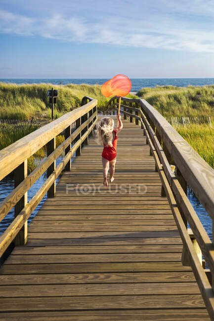 Маленькая девочка из Нью-Йорка бежит по мосту на пляж с красной рыболовной сетью — стоковое фото