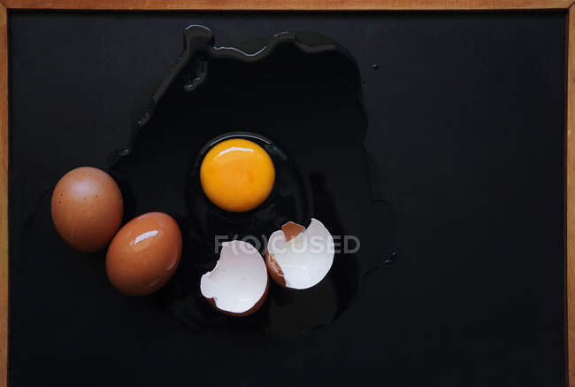 Ovo quebrado com ovos castanhos inteiros em um fundo preto, vista superior — Fotografia de Stock