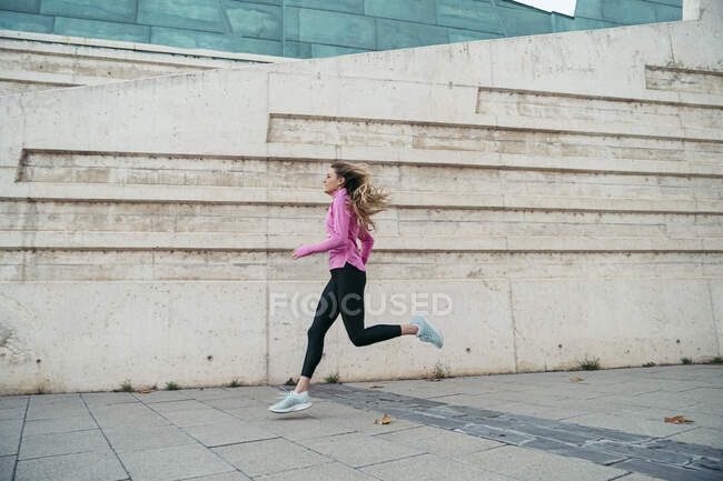 Side view of woman running along modern wall — Stock Photo