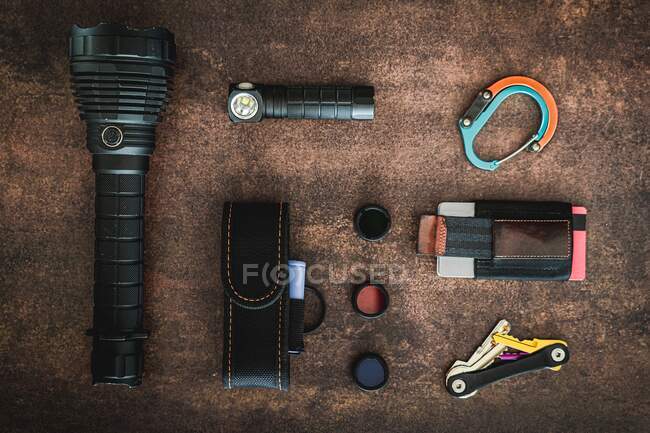 An amount of some EDC (Everyday carry) items on a wooden surface. There are some flashlights, a clip, a minimalist wallet, 3 flashlight filters, a flashlight cover and a key organizer keychai — Stock Photo