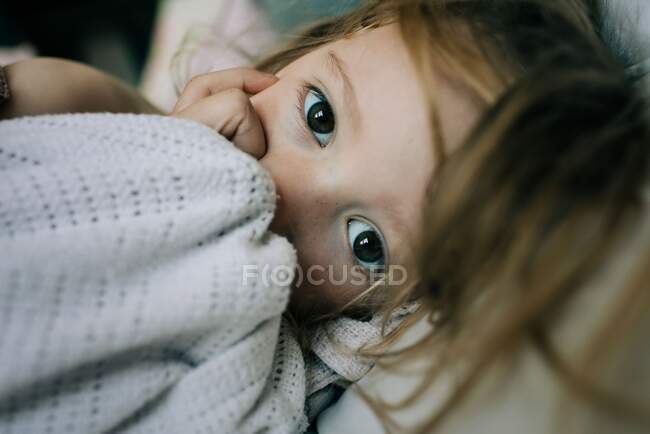 Close up portrait of young girl holding a comforter and sucking thumb — Stock Photo