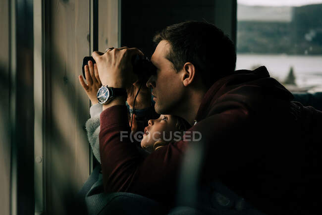 Father and daughter looking out the window with binoculars at nature — Stock Photo