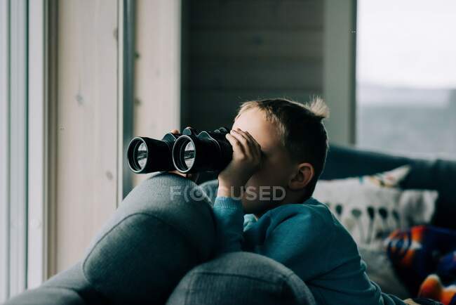 Young boy looking through binoculars at nature from a cosy cabin — Stock Photo