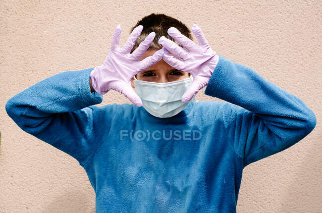One blonde boy wearing latex gloves and face masks is showing the way he protects himself from coronavirus, bacterias, virus, fungus, etc. He is scared to be infected in pandemic. Horizontal — Stock Photo