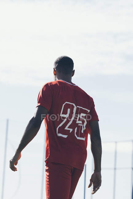 Back view of African American soccer player walking on grass pitch — Stock Photo