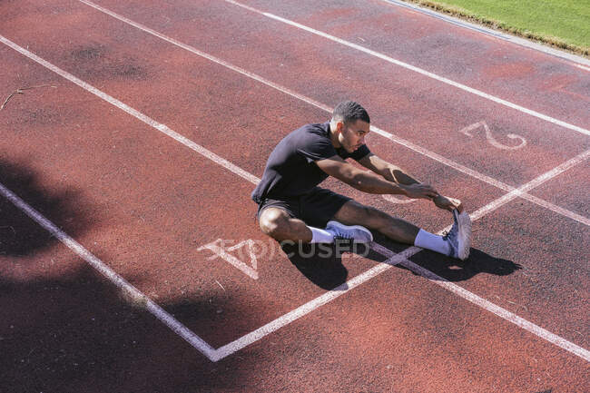 Atleta afro-americano que se estende na pista de corrida — Fotografia de Stock