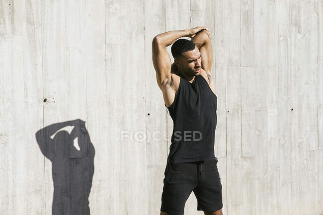 Athlète masculin afro-américain s'étirant contre un mur en béton — Photo de stock