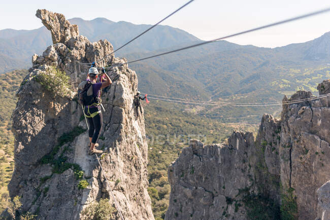 Woman with helmet, harness and backpack. Walking over the abyss on a Tibetan bridge. doing via ferrata in the mountains. — Stock Photo