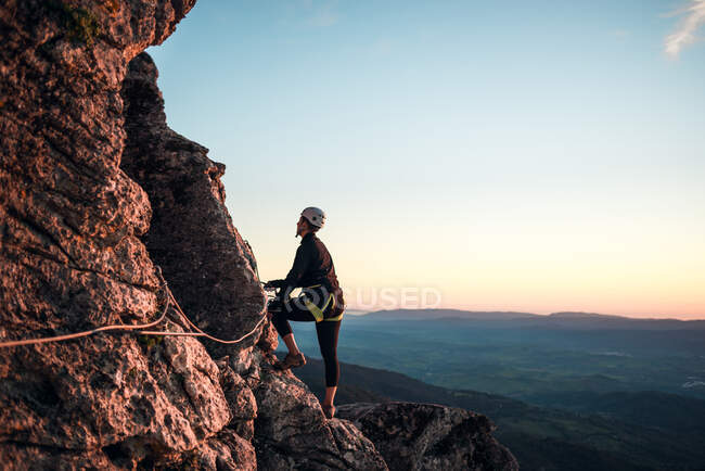 Mulher alpinista com capacete e arnês. Silhueta ao pôr-do-sol na montanha. Perfil. A descansar a olhar para a rota de escalada. Fazendo via ferrata nas montanhas. — Fotografia de Stock