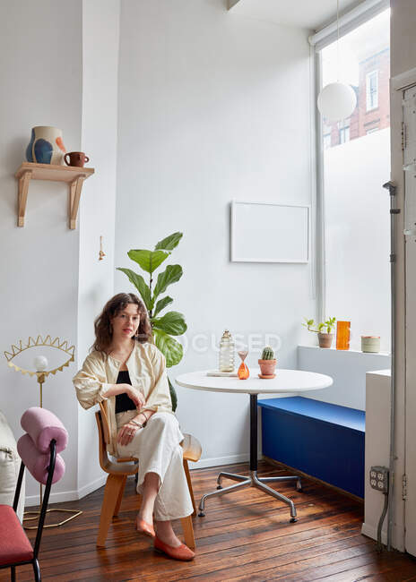 Porträt einer Frau, die an Tisch, Fenster und Bankett in der Ecke sitzt — Stockfoto