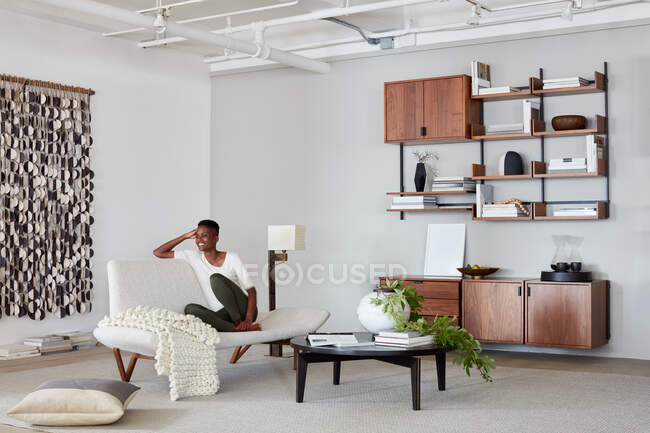 Woman on couch in clean, modern living space with console and shelving — Stock Photo