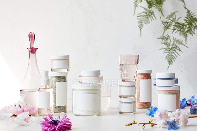 Crema cosmética, flores y pétalos sobre un fondo blanco - foto de stock