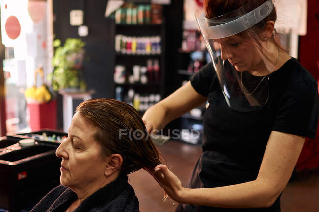 Cabeleireiro penteia um cliente com um escudo facial — Fotografia de Stock