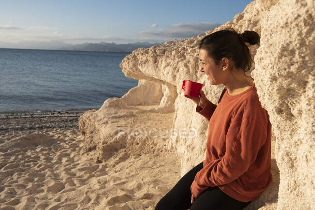 Una mujer con una taza en la mano en la playa de una isla - foto de stock