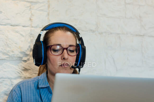 Женщина работает со своим ноутбуком и сосредоточена на прослушивании в наушниках — стоковое фото