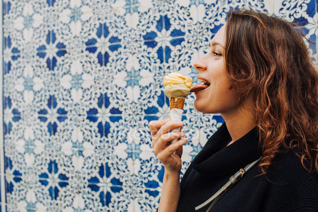 Jeune femme lécher la crème glacée tout en se tenant à un mur carrelé à Lisbonne — Photo de stock