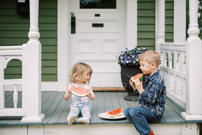 Brother and sister eating watermelon together on their front porch — Stock Photo