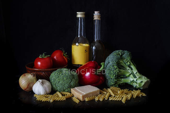 Натюрморт, помідор, брокколі, олія та макарони на чорному студійному фоні — стокове фото