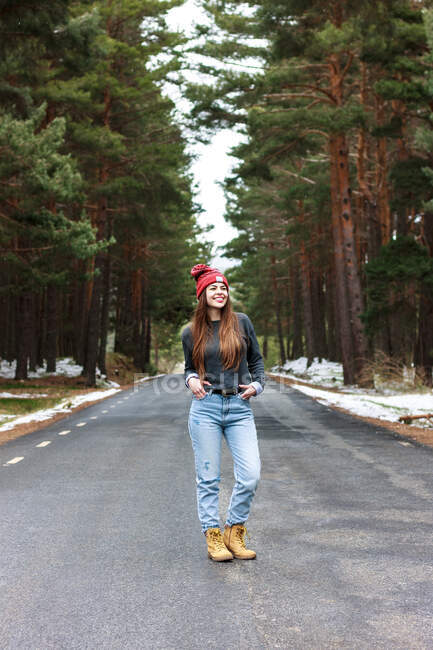 Glückliches junges Mädchen, das inmitten einer einsamen Straße im verschneiten Wald spaziert. — Stockfoto