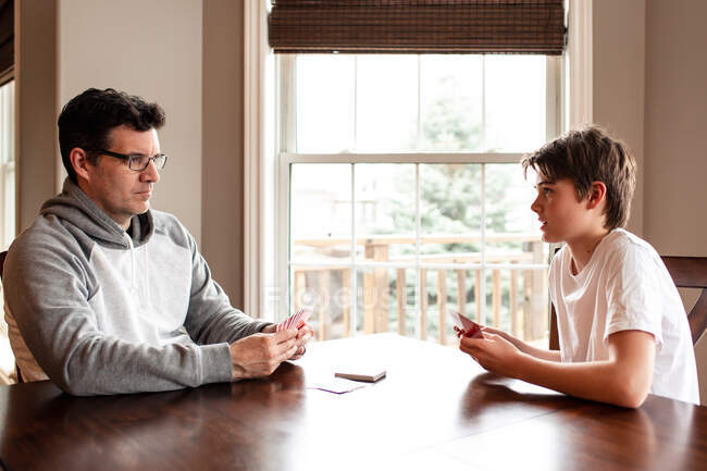 Adolescente menino e seu pai jogando cartas na mesa juntos. — Fotografia de Stock