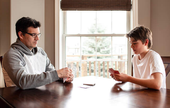 Adolescente y su padre jugando a las cartas en la mesa juntos. - foto de stock