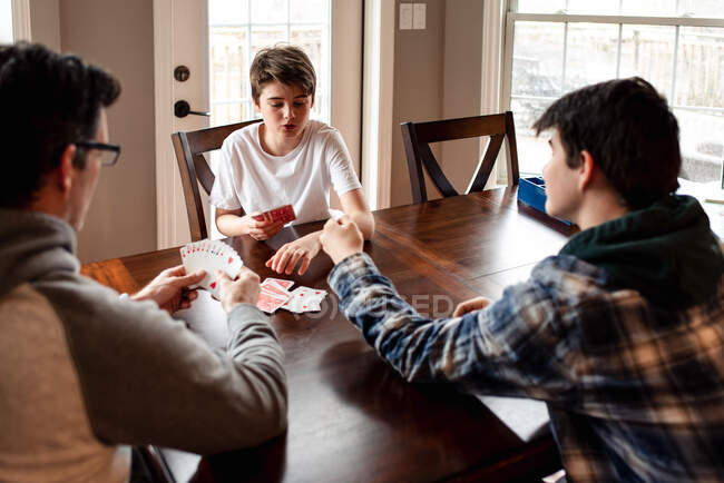 Father and adolescent sons playing cards at the table together. — Stock Photo