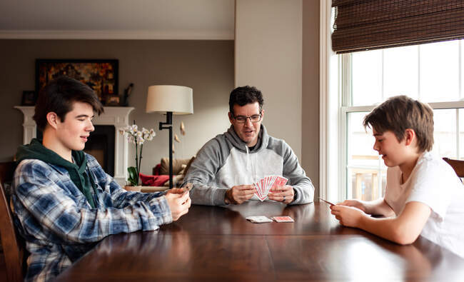 Father and adolescent sons playing cards at the table together. — Stock Photo