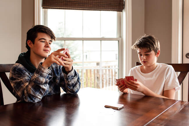 Dos adolescentes jugando a las cartas en la mesa de la cocina juntos. - foto de stock