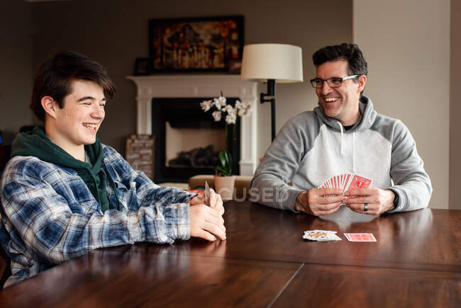 Батько і підліток син сміється, коли вони грають карти за столом . — стокове фото