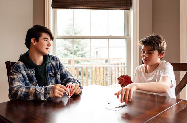 Dois meninos adolescentes jogando cartas na mesa da cozinha juntos. — Fotografia de Stock