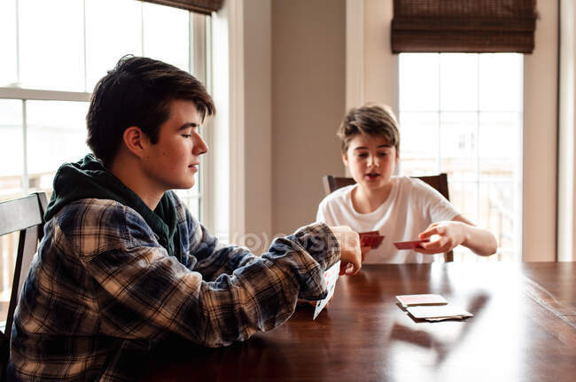 Dos adolescentes jugando a las cartas en la mesa de la cocina juntos. - foto de stock