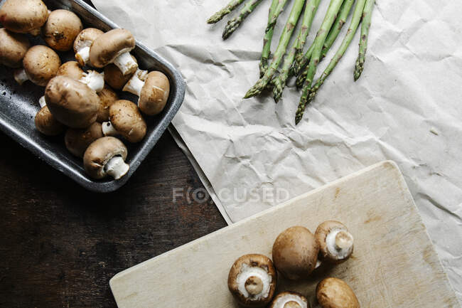 Vista superior de champiñones reales crudos y tallos de espárragos verdes en pergamino preparado para cocinar una cena saludable - foto de stock