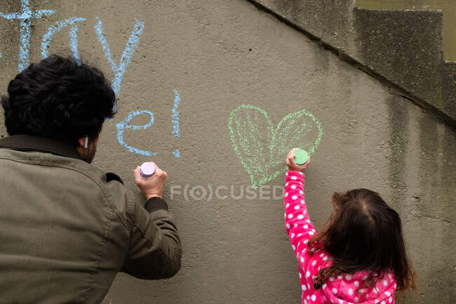 Padre e hija dibujan mensajes alentadores con tiza - foto de stock