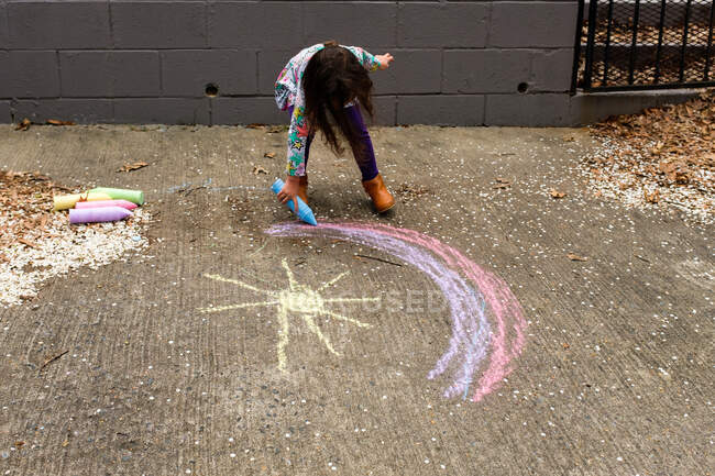 Kleines Mädchen zeichnet Regenbogen mit Kreide — Stockfoto