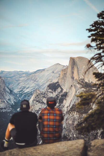 Двоє людей, які сиділи на скелі, насолоджуючись краєвидом півкупола. — стокове фото