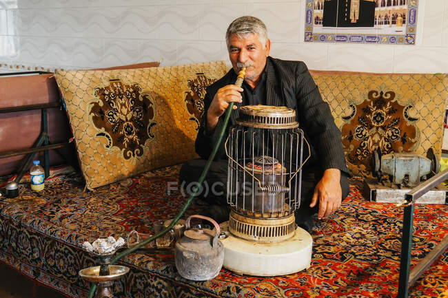 El hombre fuma una pipa en un mercado de Teherán - foto de stock